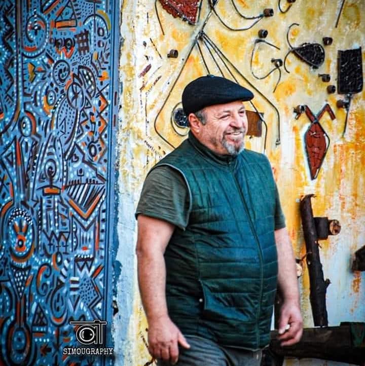 Portrait de Djamel Metref devant une porte et un mur aux motifs colorés.