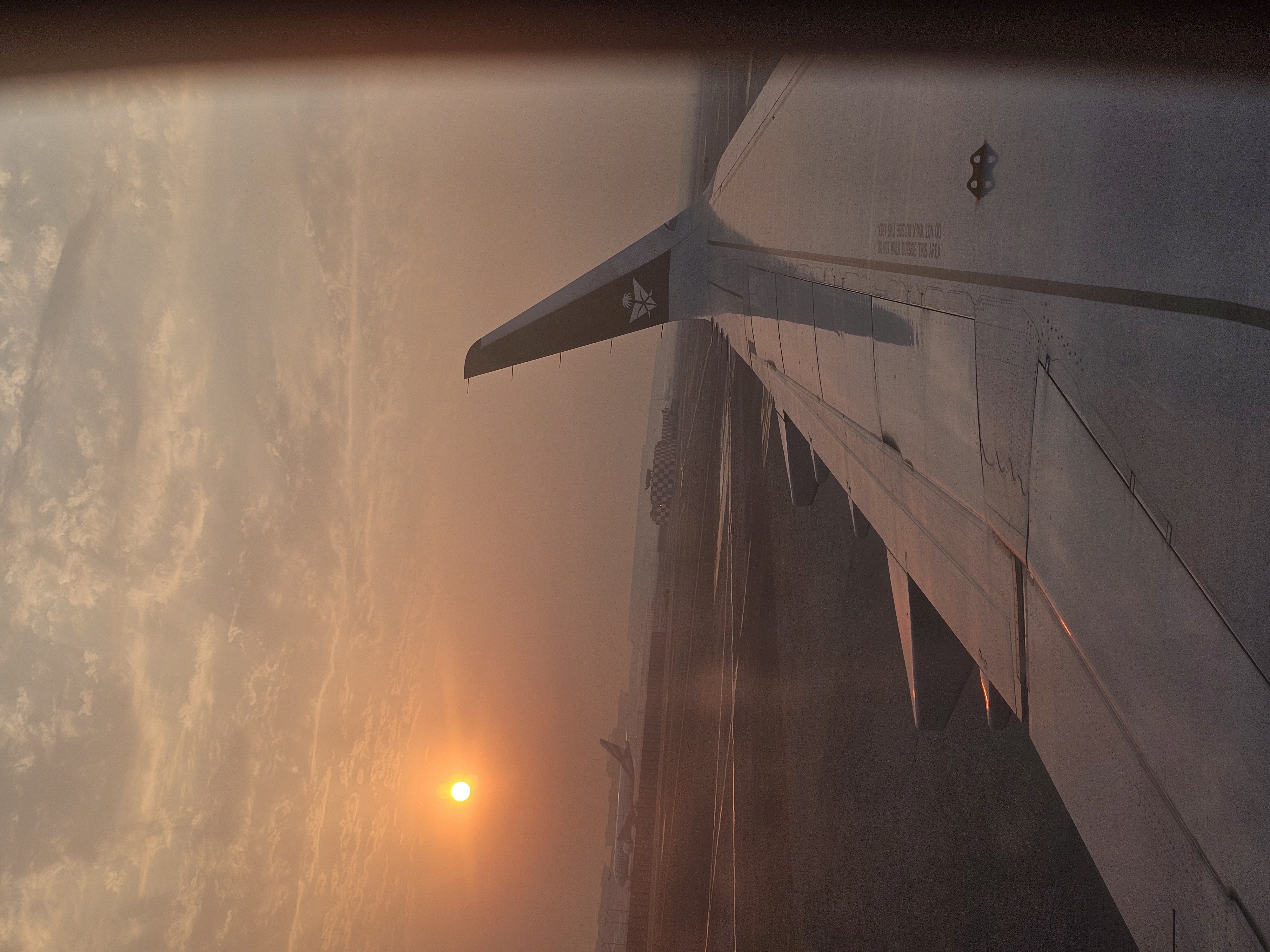 Une aile d’avion vue à travers un hublot au soleil couchant.