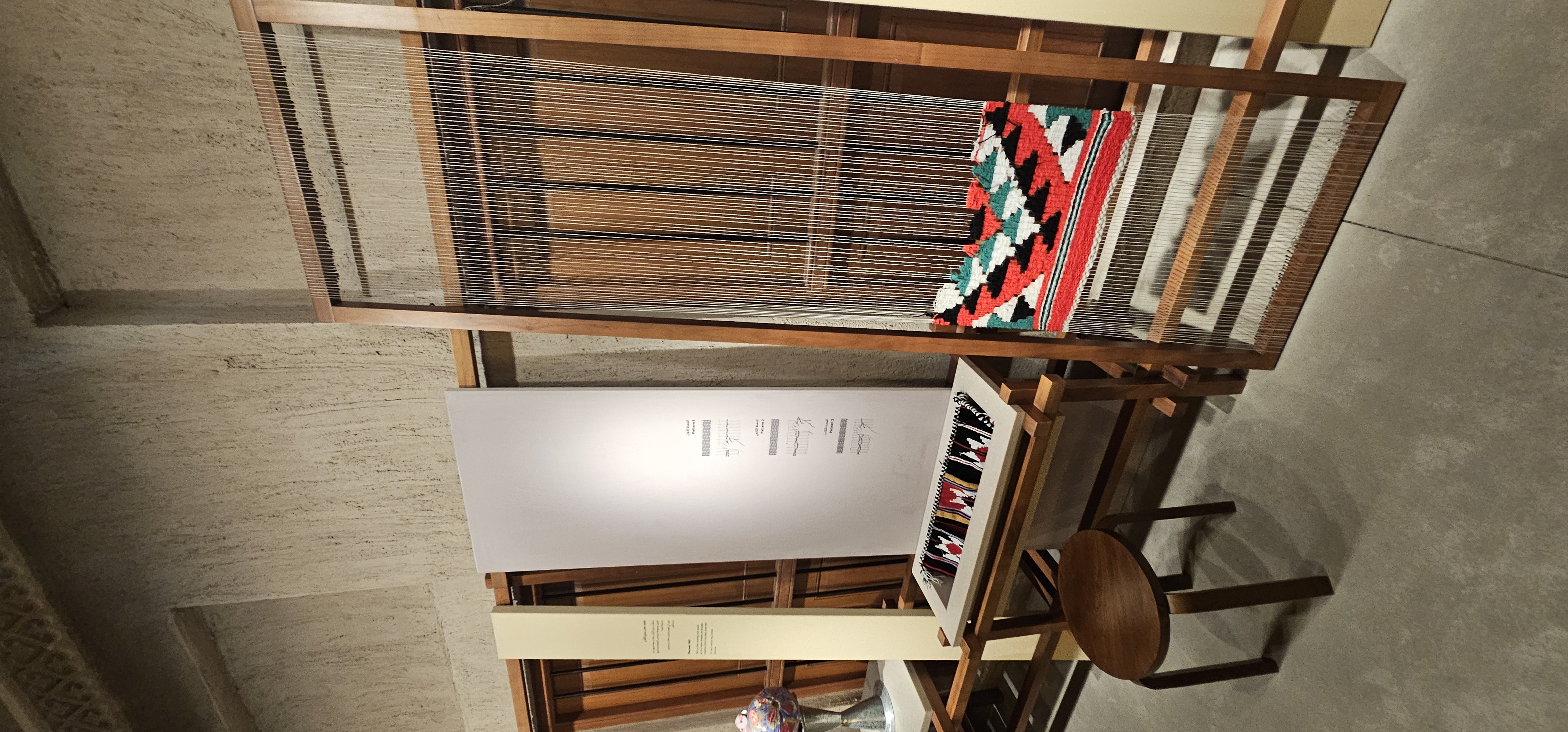 Un métier à tisser en bois porte un ouvrage aux motifs rouges, noirs et verts.