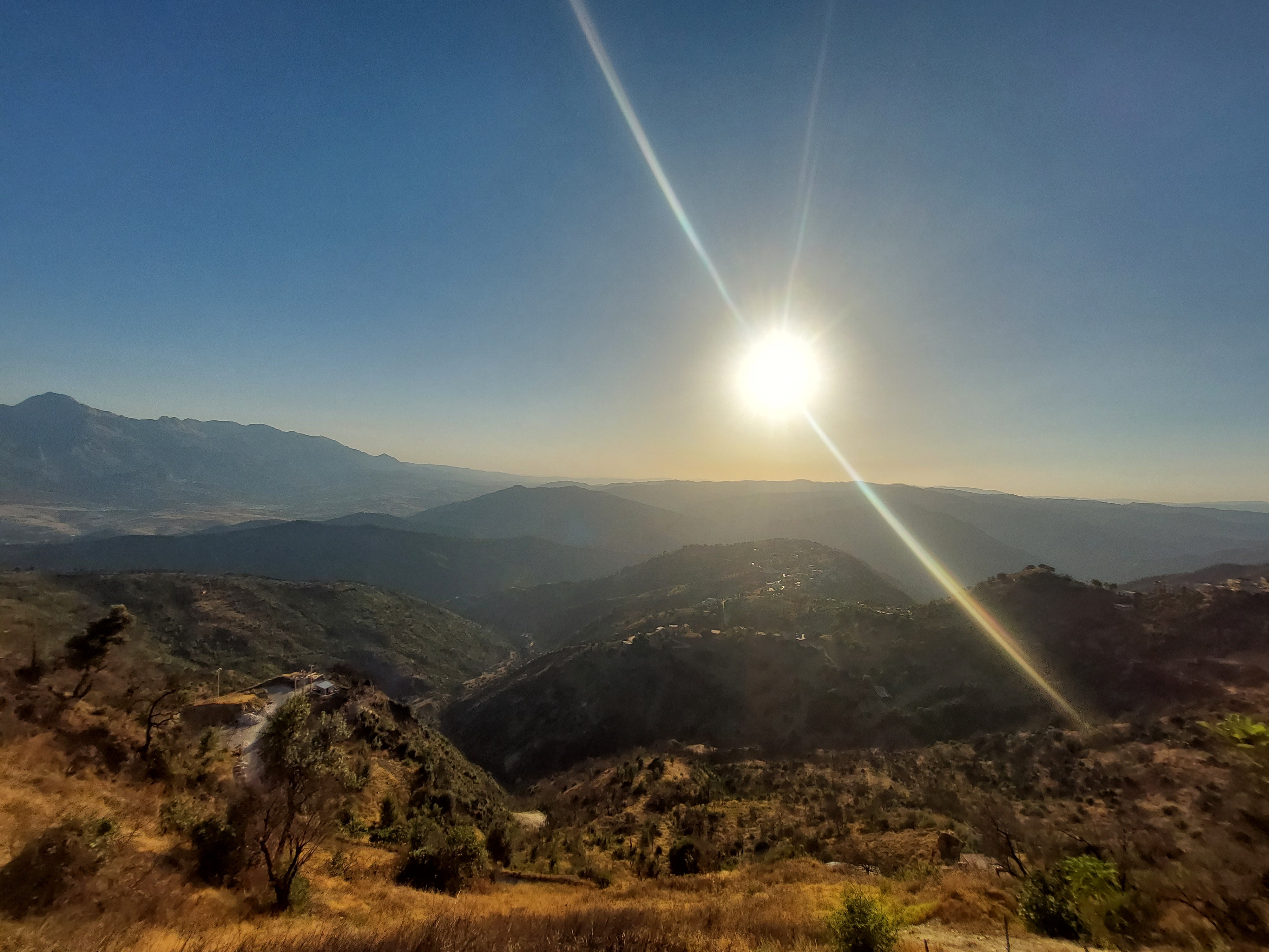Le soleil au-dessus des collines et d’un chemin dans un paysage montagneux.